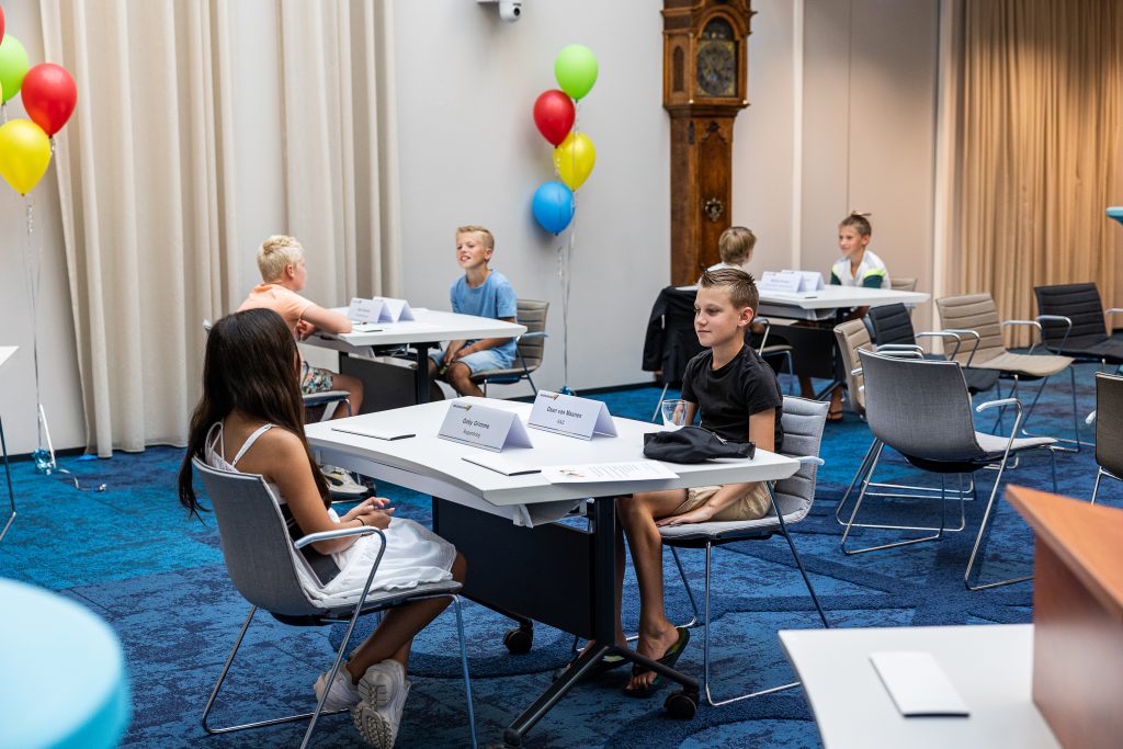 kinderen van kindercomité aan tafels in raadzaal