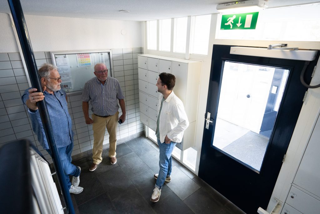 Vertegenwoordigers van de VvE staan in de centrale hal van hun flatgebouw. Zij zijn in gesprek met een energiecoach.