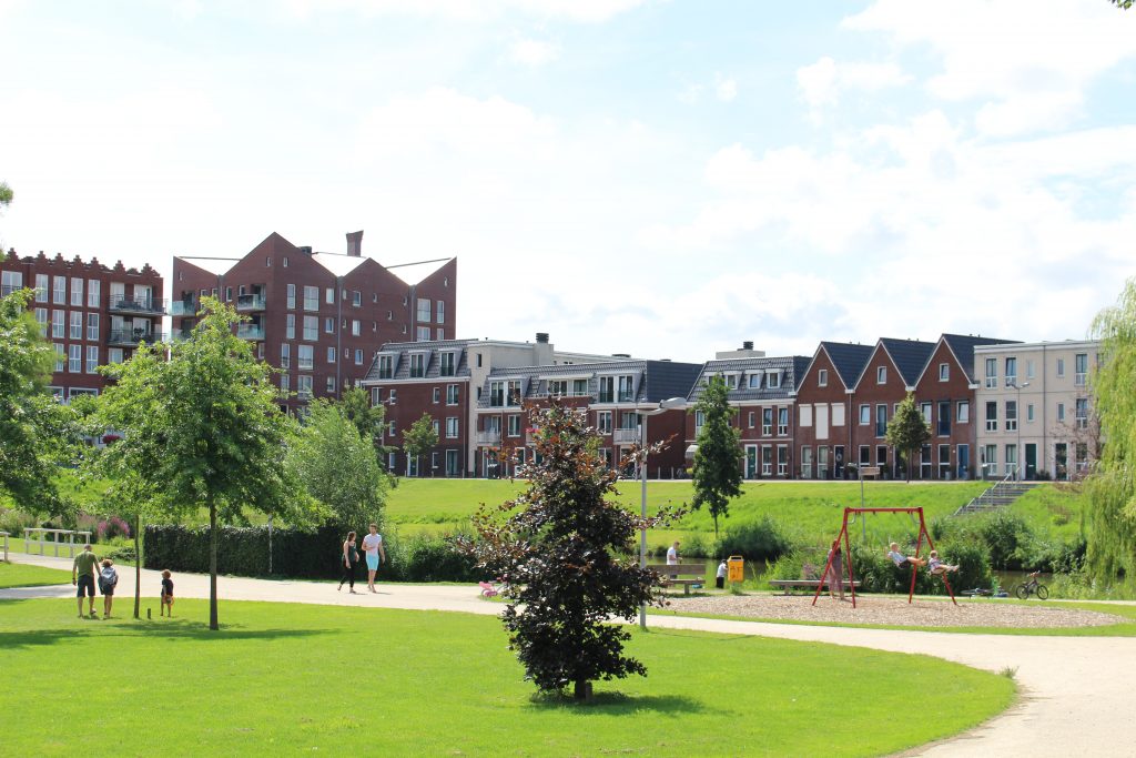 Warnaarplantsoen met de Kroon op de achtergrond, lopende en spelende mensen en groen grasveld met bomen en huizen