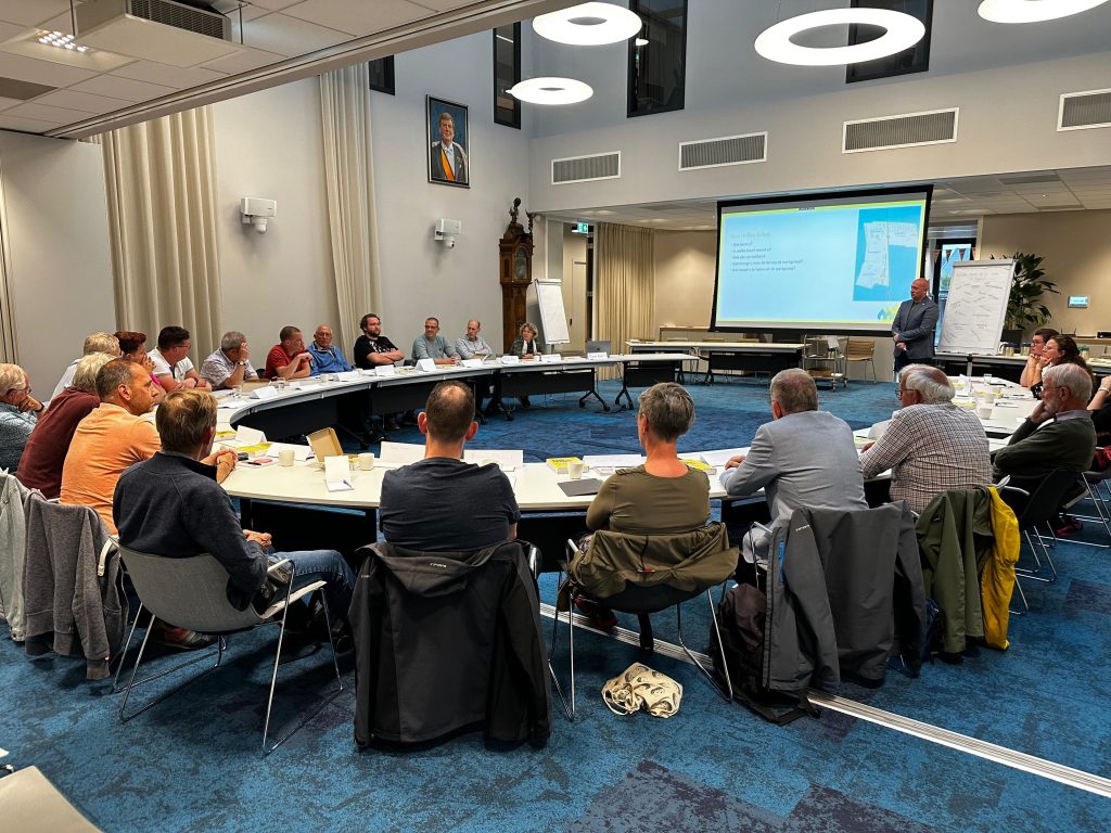 mensen zitten in de raadzaal van de gemeente Waddinxveen aan een ronde tafel
