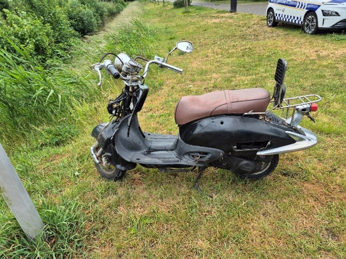 Zwart bruine scooter geparkeerd in de grasrand aan de Zevende Tochtweg.