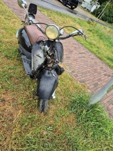 Voorkant van de zwart bruine scooter geparkeerd in de grasrand aan de Zevende Tochtweg.