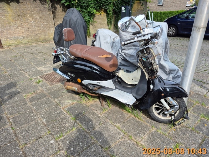 Een zwarte scooter met bruin zadel zonder kenteken, Floriserf vlakbij nummer 2 op de parkeerplaats.