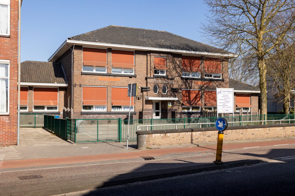 schoolgebouw met speelplaats en hekken en oranje zonnewering naar beneden