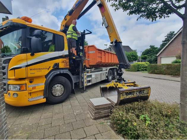 Vrachtwagen tilt met grijparm tegels op van de stope die een inwoner heeft aangeboden